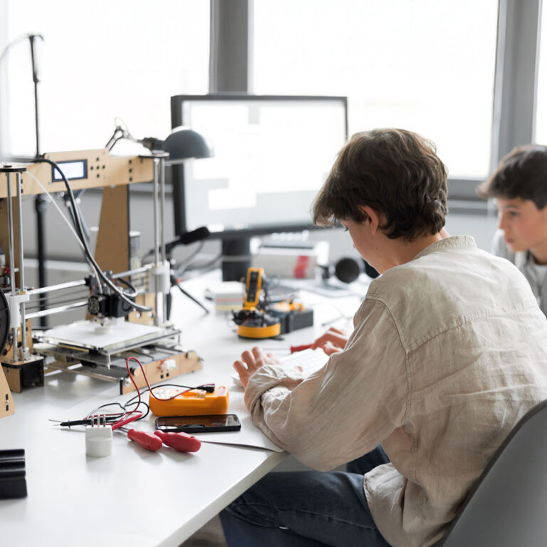 Students sitting at desk in the lab and learning 3D printing together, one is typing and the other is assisting him